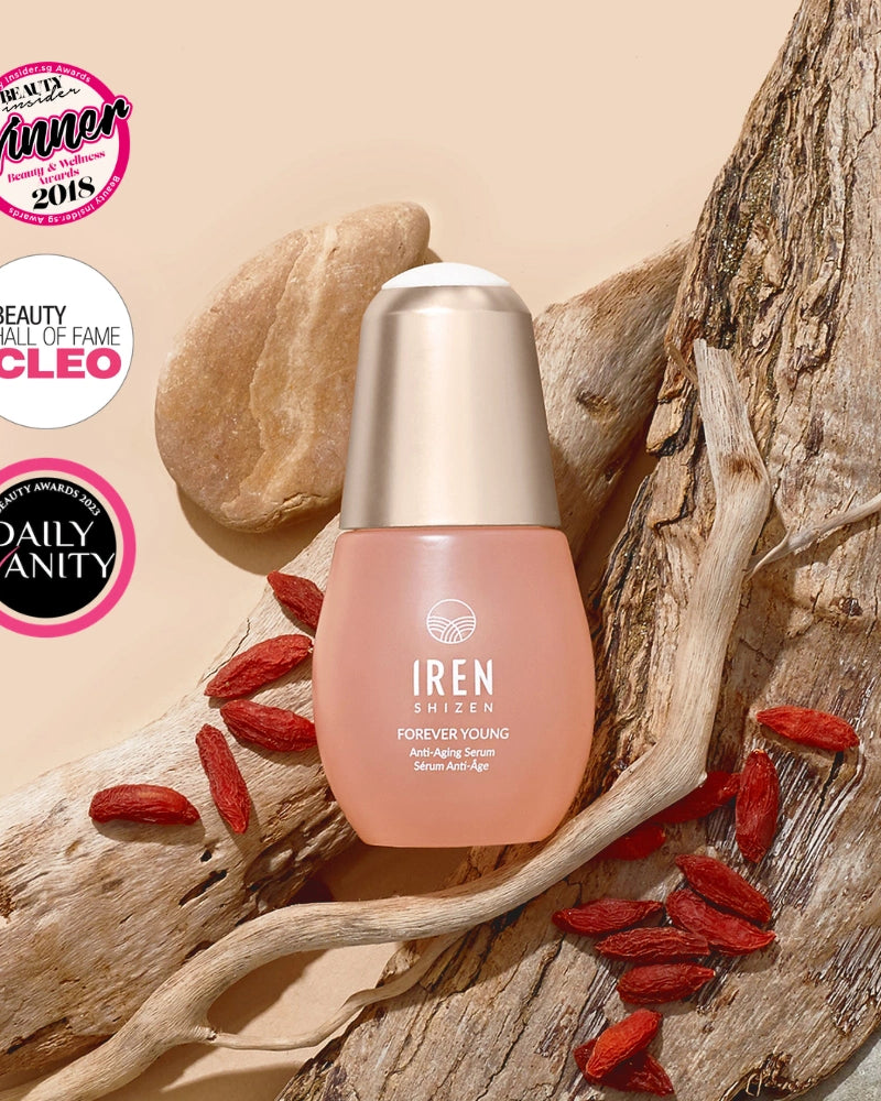 A bottle of IREN Shizen FOREVER YOUNG Anti-Aging Serum rests on driftwood with goji berries, framed by three award badges in the top left, emphasizing its anti-aging properties and collagen support. #all-groups