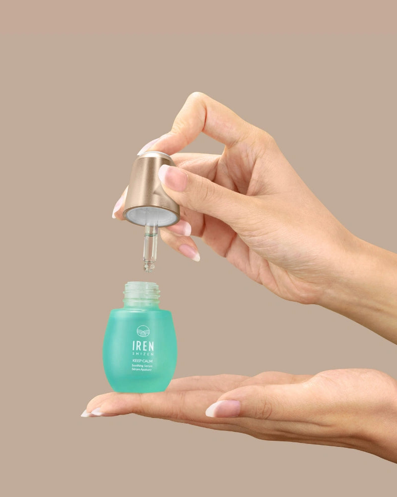 A person dispenses KEEP CALM Soothing Serum by IREN Shizen from a dropper bottle onto their palm against a plain beige background. #all-groups