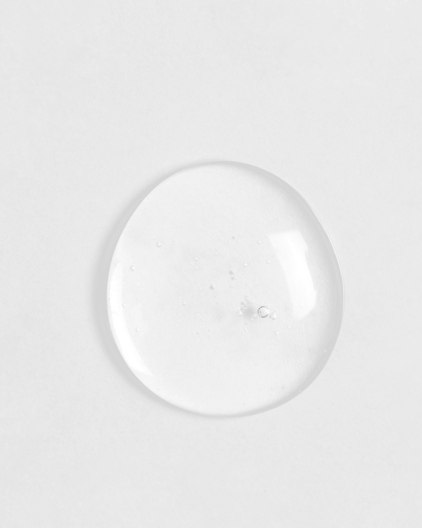 A single, clear droplet of IREN Shizen's LIFT & FIRM Anti-Aging Duo Serum on a white surface.