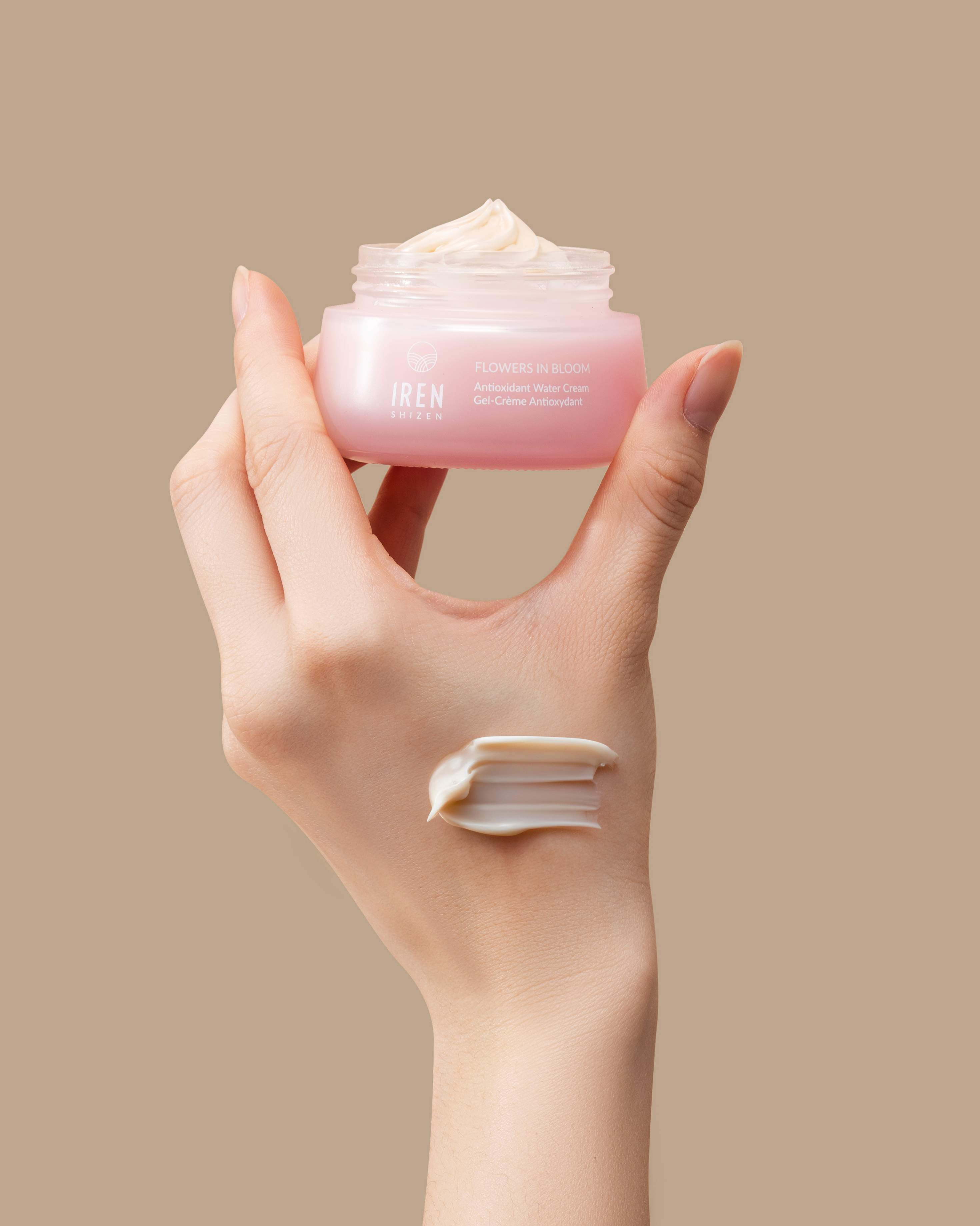 A hand holds a jar from the IREN Shizen MOISTURE SANDWICH Skincare Kit, with a swipe of cream—formulated to boost hydration and support the moisture barrier—applied to the back of the hand, set against a beige background.