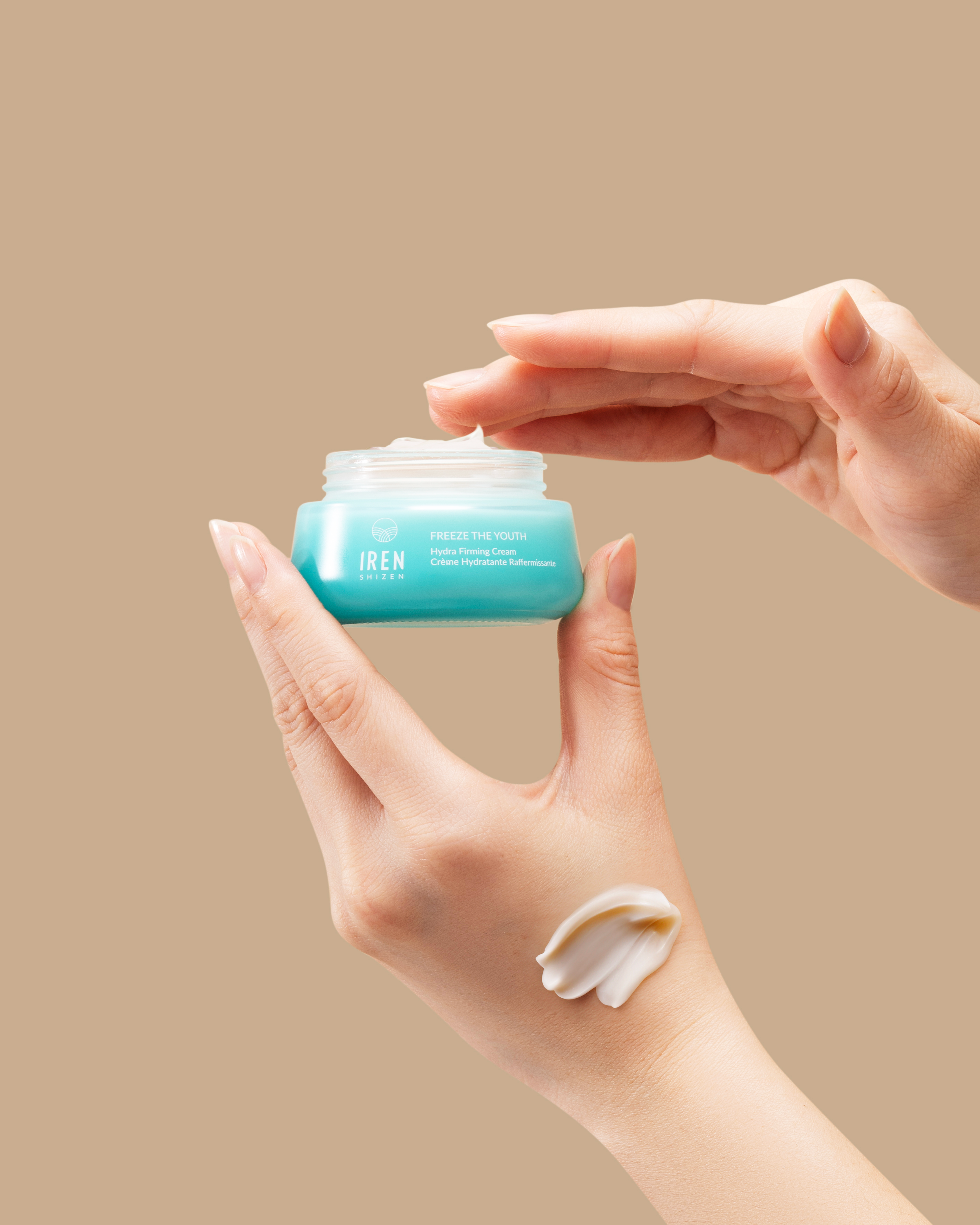 A hand holds a blue jar from the IREN Shizen MOISTURE SANDWICH Skincare Kit while another dips in; cream is swatched on the lower hand, showcasing hydration and a strengthened moisture barrier against a beige background.