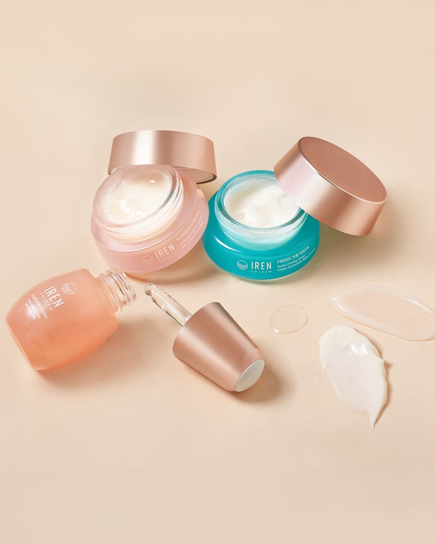 The MOISTURE SANDWICH Skincare Kit by IREN Shizen, featuring pink, blue, and peach containers with visible product smears on a beige surface, showcases hydration and serum absorption. A dropper is placed nearby.