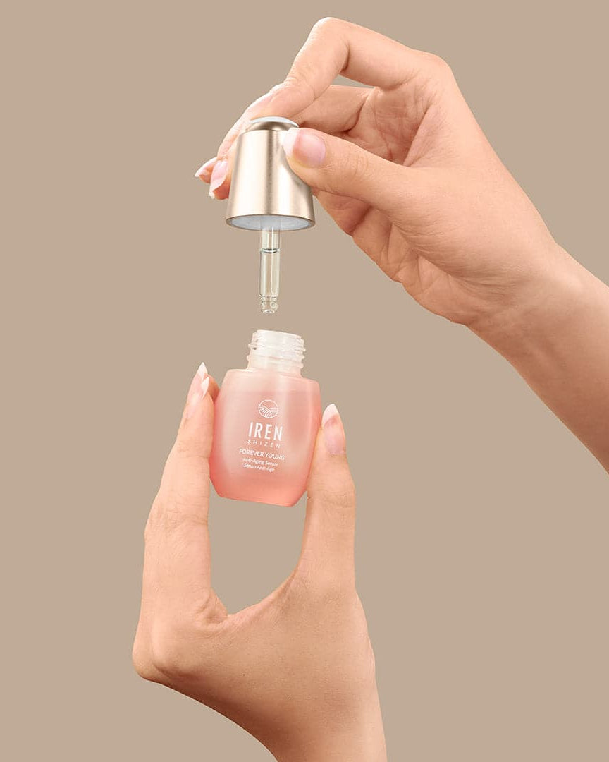 A hand is holding a bottle of IREN Shizen customised FOREVER YOUNG Anti-Aging Serum on a beige background. #all-groups