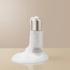 A white bottle of IREN Shizen START AFRESH DAILY Enzyme Powder Wash, a gentle exfoliant, is placed on a beige surface with white foam around it and a neutral background.