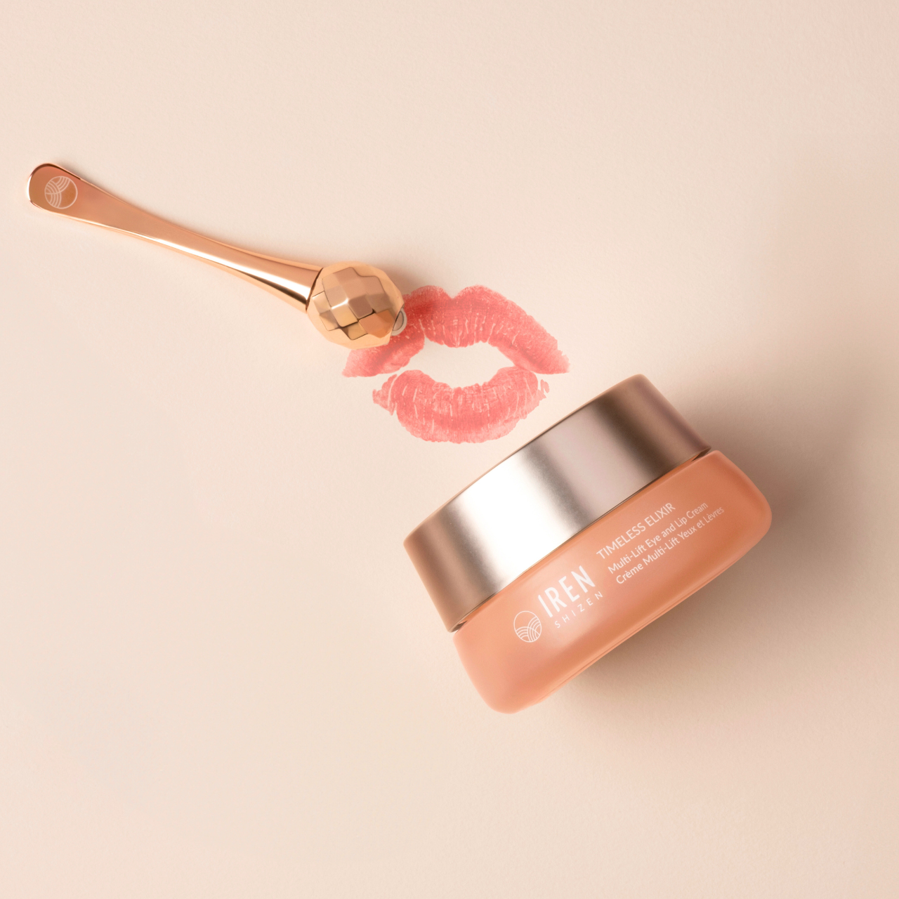 A jar of TIMELESS ELIXIR Multi-Lift Eye and Lip Cream by IREN Shizen, infused with Bakuchiol, sits next to a gold applicator and a lipstick kiss mark on a light beige background.