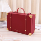 A FOR BELOVED ONES Xmas Luggage Gift Box by IREN Shizen, featuring red with gold corner accents and a handle, sits on a table. The box displays the text "Special Gift Just For You.