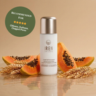A bottle of Fast Bundle's Cloud Cleansing Kit is surrounded by papaya slices and wheat, with a green badge recommending its gentle enzyme cleanser for oiliness, dullness, and clogged pores.