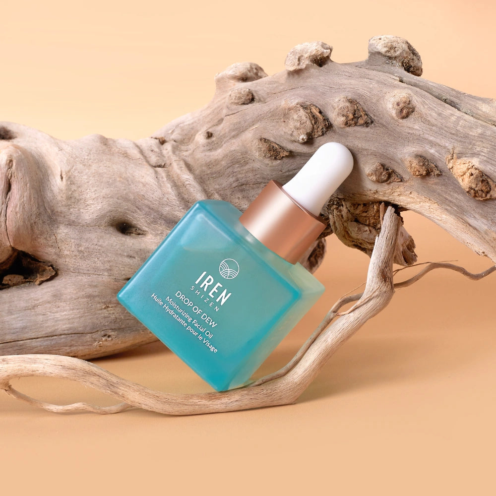 A blue dropper bottle labeled "IREN Shizen" containing DROP OF DEW Moisturizing Facial Oil for skin barrier repair rests on textured driftwood against a beige background.
#all-groups