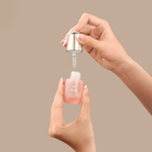 A person holds a small bottle of IREN Shizen FOREVER YOUNG Anti-Aging Serum in one hand and removes the dropper cap with the other, showcasing its anti-aging benefits against a plain beige background.