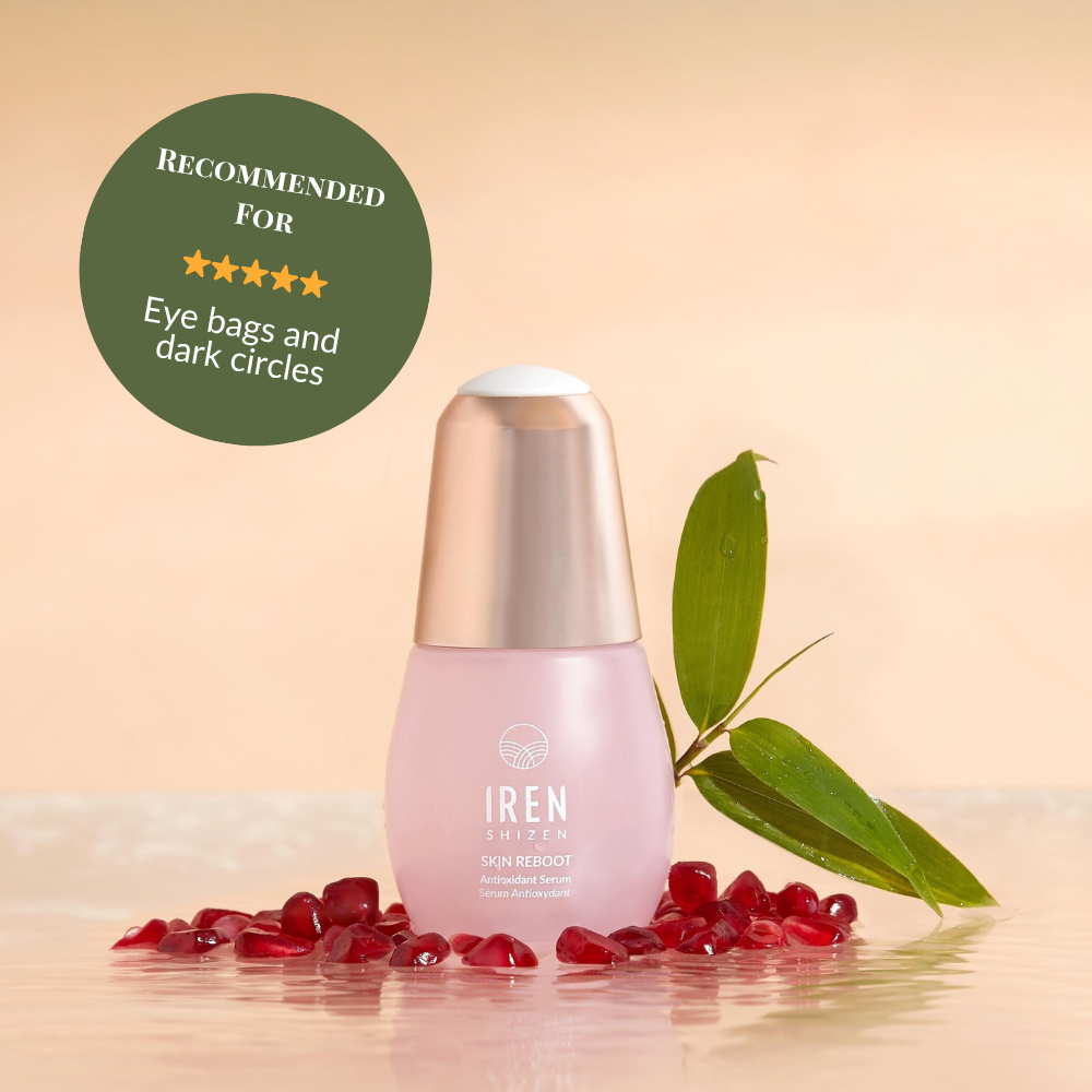 A bottle of SKIN REBOOT Antioxidant Serum by IREN Shizen is shown with pomegranate seeds, a green leaf, and a badge that recommends it for reducing dark circles and eye bags. #show-lang-en