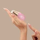 A person dispenses IREN Shizen’s SKIN REBOOT Antioxidant Serum, a pink formula, onto their fingertip from a small bottle against a plain beige background.