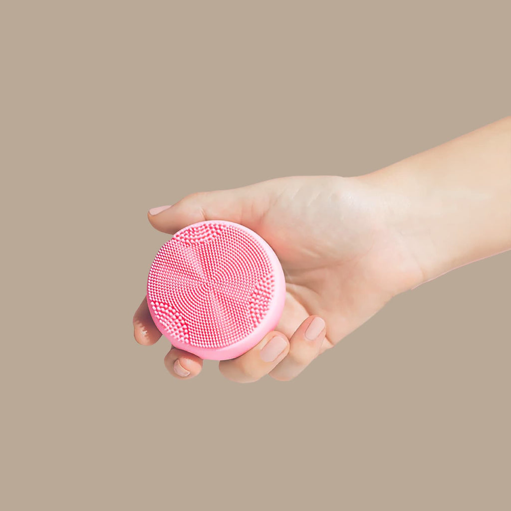 A person's hand holding a SKIN GENIE PRO Cleansing Brush for customized Japanese skincare on a beige background.