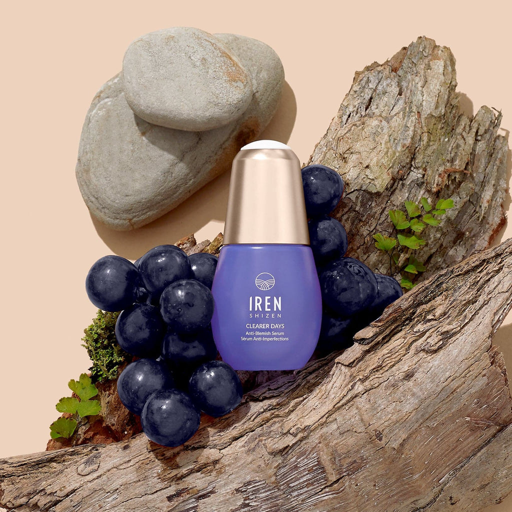 A bottle of CLEARER DAYS Anti-Blemish Serum with grapes and grapes on top of a piece of wood, showcasing Japanese skincare.