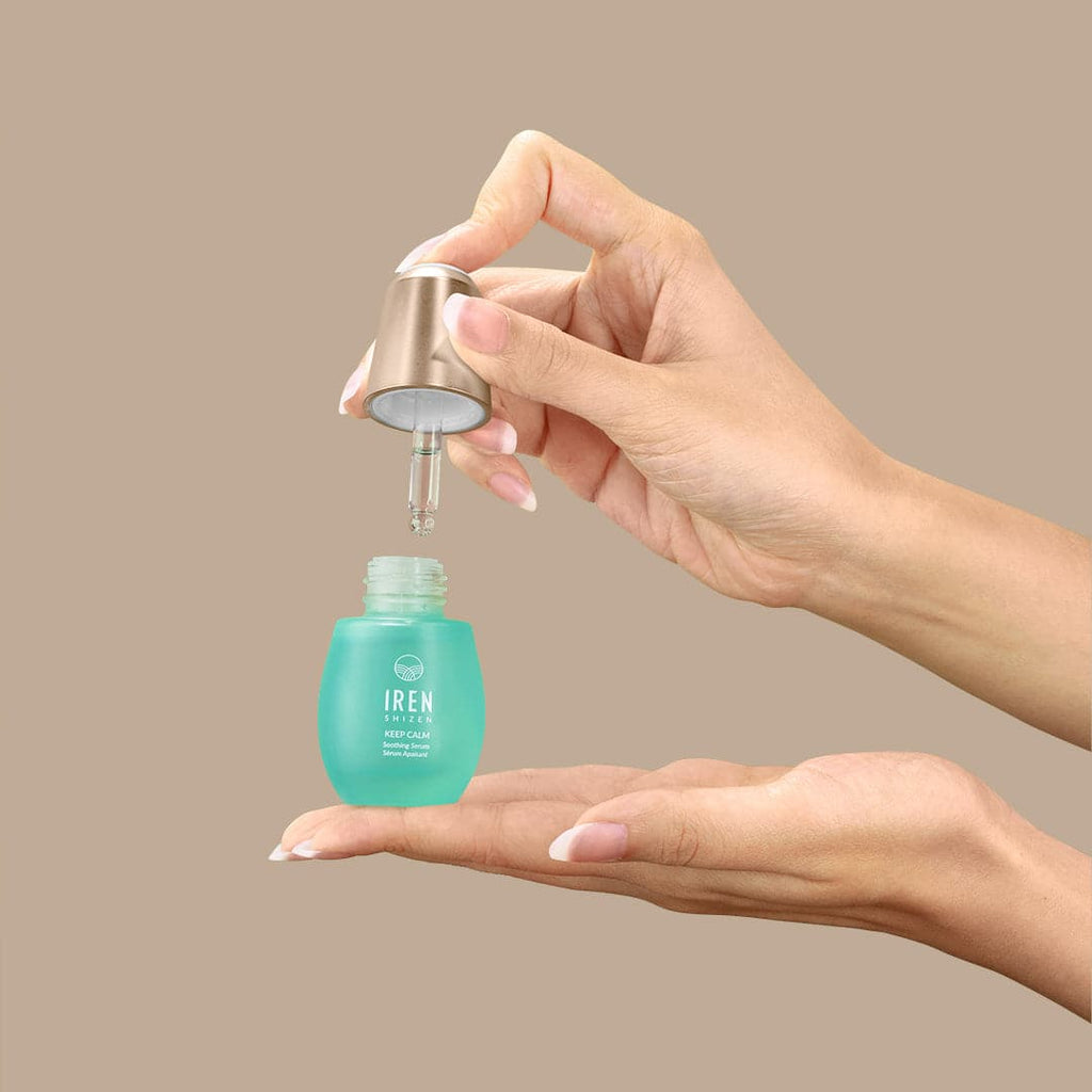 A woman's hand holding a bottle of customised KEEP CALM Soothing Serum by IREN Shizen, inspired by Japanese and onsen skincare.